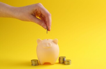Financial savings. Woman putting coin into piggy bank on yellow background, closeup