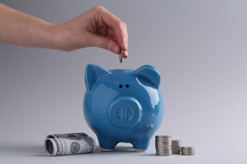 Financial savings. Woman putting coin into piggy bank on grey background, closeup