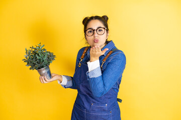 Young caucasian gardener woman holding a plant isolated on yellow background looking at the camera...