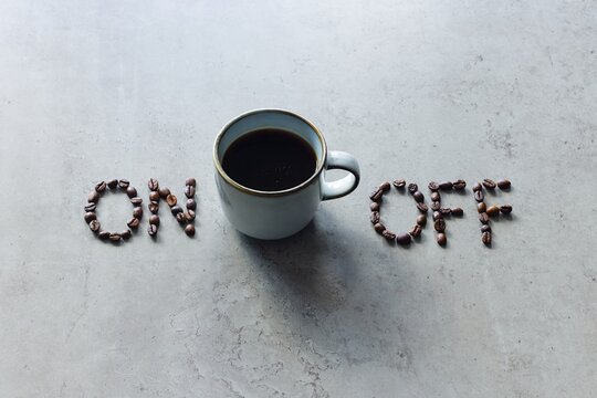 The image depicts the words "on" and "off" arranged with coffee beans, with a cup of freshly brewed black coffee in between. It symbolizes activating the mind, body, and person to stimulate action.