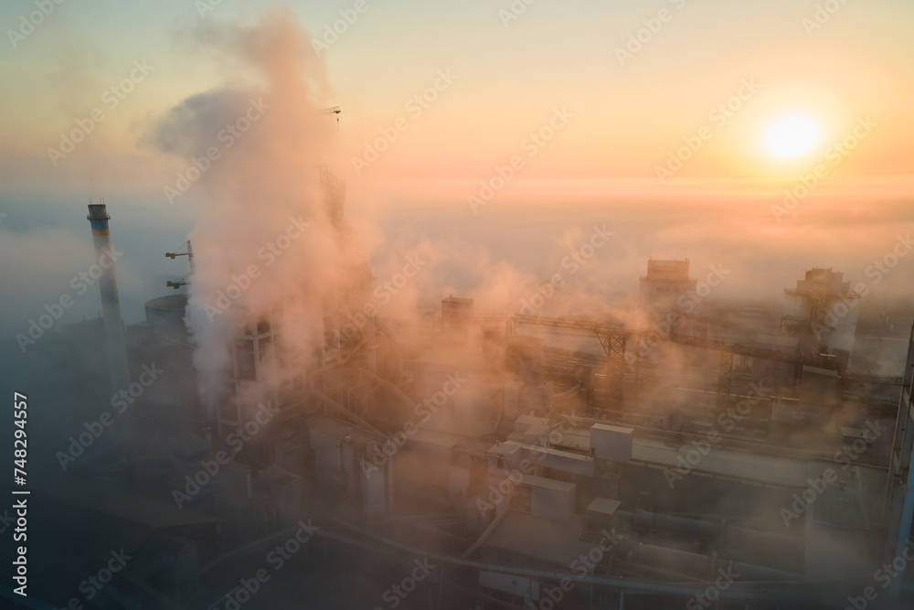 Poster Aerial view of cement factory with high concrete plant structure and tower crane at industrial manufacturing site on foggy evening. Production and global industry concept