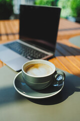 A cup of aromatic coffee on the background of a laptop on a summer terrace. Work in a cafe. Remote work online.