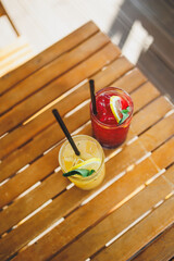 Two glasses of cool refreshing fruit lemonade stand on a wooden table. Summer soft drinks