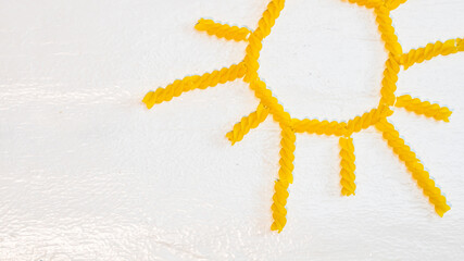 Obraz premium Sun made from fusilli pasta, green field made from green spiral pasta on white background