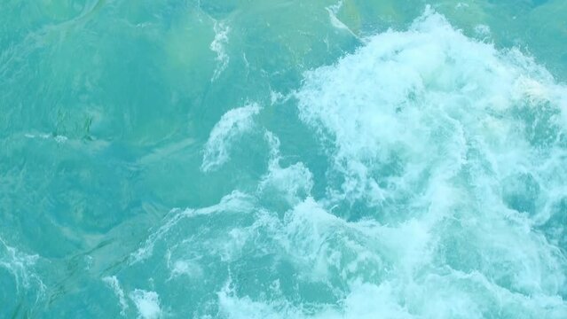 Top view of a rapidly seething stream of water. Big powerful ocean waves. White foam and water ripple. Foaming and splashing in the ocean. Strong flow of a mountain river. Translucent sea bottom