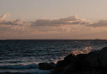 Fototapeta premium sunset on the beach with crashing waves on the rocks with ship on the horizon 