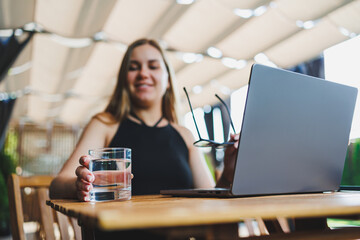 A glass of water on the background of a laptop on a summer terrace. Work in a cafe. Remote work online.