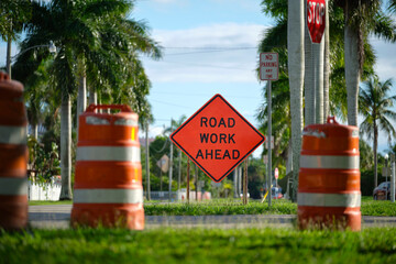 Road work ahead sign and barrier cones on street site as warning to cars about construction and...