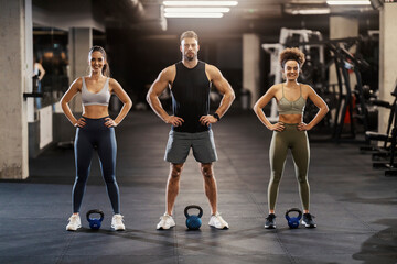 Sporty friends standing in a gym and posing with kettlebells.