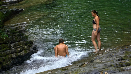 Woman and teenage boy bathing in splashing waterfall in tropical forest. Creative. Happy family enjoying fresh water from flowing waterfall in jungle.