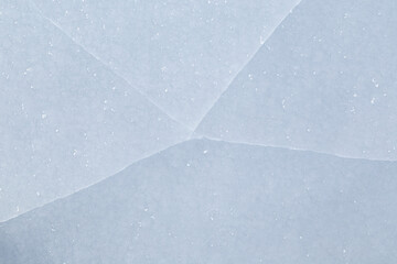 Close-up of cracked ice on a frozen lake in the winter, viewed from above. Abstract textured full frame background. Copy space, top view.