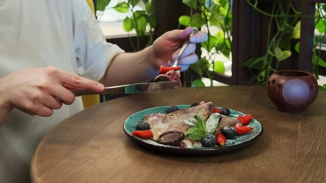 Young woman impales piece of pancake on fork closeup. Yong woman visitor prepares for delightful degustation experience in restaurant