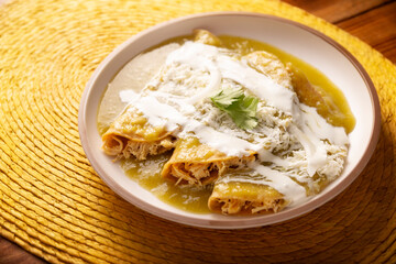 Green enchiladas. Typical Mexican dish made with a folded or rolled corn tortilla filled with shredded chicken and covered with spicy green sauce, cream, grated cheese and onion.