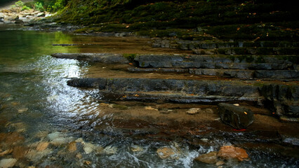 Clear stream running through stone boulders. Creative. Calm river flowing on stone bottom in slow motion.