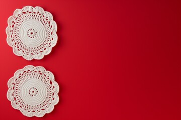 Two white crochet napkins against a red background with copy space.