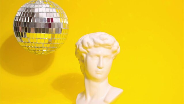 Stop motion animation of an antique statue of a man next to a disco ball moving on a yellow background