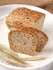 Wheat and rye sourdough mold bread with sesame seeds and flaxseed. Traditional homemade bread from Poland. Rustic arrangement with white wooden tray and grain ears.