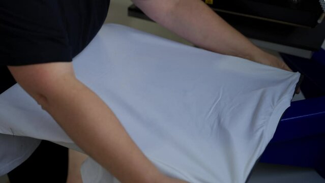 Preparing T-Shirt for Printing. Person holding white t-shirt on printing press for customization.