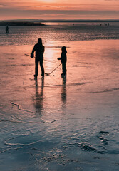 persons playing ice hockey on a frozen lake at sunset