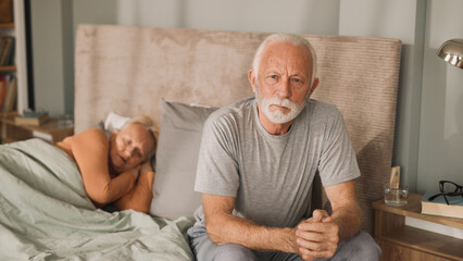 Worried senior man sitting on bed in his bedroom