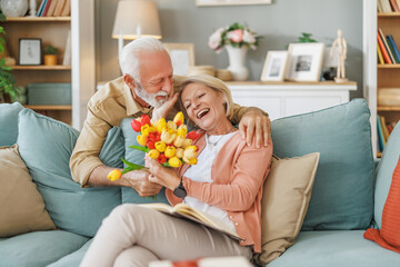 Anniversary surprise - Senior man presents flowers to his wife at home