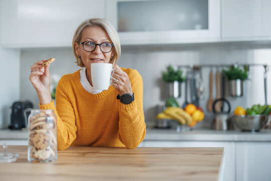 Elderly woman enjoying cookies and coffee in kitchen