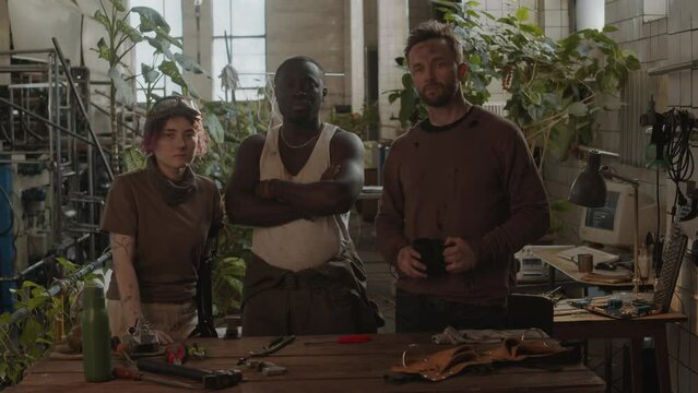 Group portrait of three confident survivors wearing worn clothes standing in post apocalypse shelter and posing together for cameraGroup portrait of three confident survivors wearing worn clothes stan