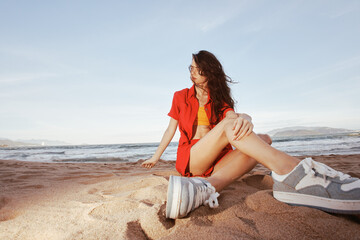 Fototapeta na wymiar Sunny Vacation: Smiling Woman in Trendy Outfit Relaxing on the Beach, Embracing Happiness and Freedom with a Carefree Attitude, Enjoying the Beautiful Nature and Serene Ocean at Sunset.