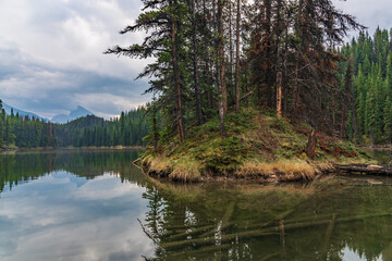 Obraz premium Moose Lake Loop Hike at Maligne Lake during fall, autumn September on cloudy day with reflection in clam water below stunning Canadian landscape scene. 