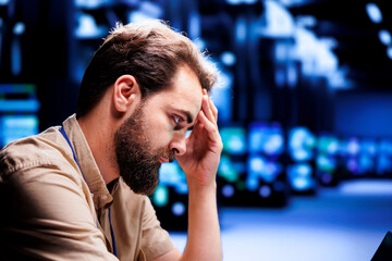 Overworked engineer struggling to maintain uptime in high tech data center. Hardworking technician upset about server hub infrastructure crashing, trying to repair equipment