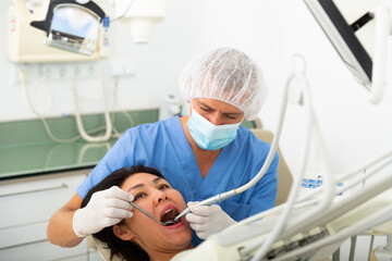 Practitioner male dentist drilling tooth to asian female patient in dental studio