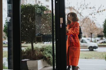 Fototapeta premium A thoughtful woman in business attire examines the cloudy outdoors through a glass door. Her contemplative stance suggests a moment of decision or reflection.