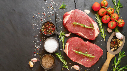 Obraz na płótnie Canvas Fresh raw beef steaks with spices and herbs on black slate.