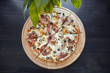 Overhead view of an artisan pepperoni and mushroom pizza on a wooden serving board, surrounded by natural green foliage