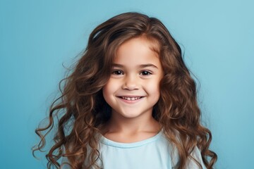 Portrait of a smiling little girl with long curly hair on blue background
