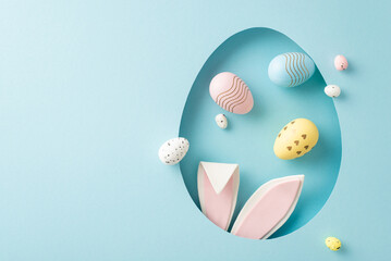 Playful Easter imagination scene: top-view photo featuring adorable hare ears peeking through egg-inspired aperture, with assorted eggs scattered on light blue surface, spot for personalized greetings © ActionGP