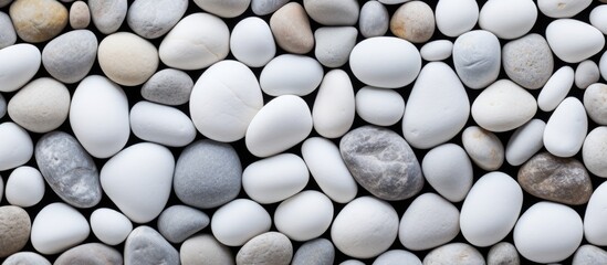 Several round, white stones are tightly packed together, creating a textured background. The rocks in various shapes and sizes are closely captured in this detailed image. - obrazy, fototapety, plakaty