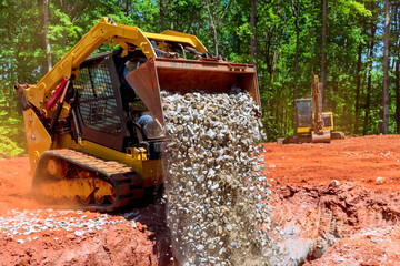 During construction, skid steer loader unloads gravel from an excavator bucket © ungvar