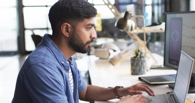 Young Asian man with beard works at computer in office setting, indicating business environment