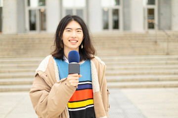 young Chinese journalist giving a live news broadcast with a microphone in his hand