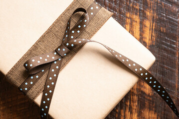 Gift wrapping, plain brown paper with a dark brown ribbon topped with a darker brown ribbon with...