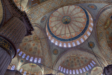 interior of the blue mosque in istanbul, with its colorful stained glass windows, its large arches, impressive ceiling with its central vault and large pillar in the foreground, Sultan Ahmed Mosque