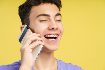 Closeup portrait of smiling boy with braces talking on mobile phone with closed eyes isolated