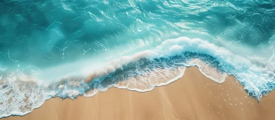 Deurstickers This aerial view showcases a beach with waves crashing onto the shore and golden sand stretching out to the endless ocean. The contrast between the majestic sand and the deep blue ocean creates a © 2rogan