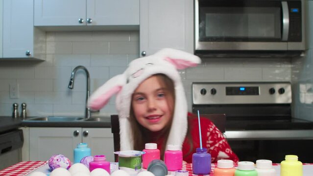 Happy Easter.Cheerful girl child with Easter bunny ears playing happily on Easter day.Kids in bunny ears and rabbit costume.Child plays in kitchen and paints Easter eggs in preparation for the holiday