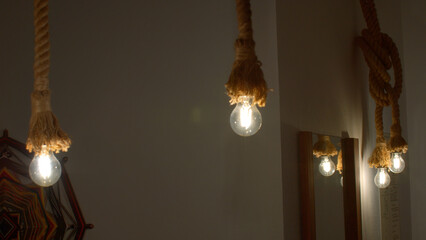 Burning stylish light bulbs decorated by ropes. Media. Stylish hanging bulbs, ethnic interior.