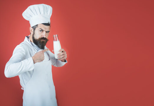 Serious chef man in uniform apron pointing finger to bottle of milk drink. Male cook in apron with bottle of kefir or yogurt. Dairy farmer products, chef recommendation. Copy space for advertising.