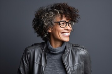 Portrait of a happy young african american woman in black leather jacket and eyeglasses, over grey background