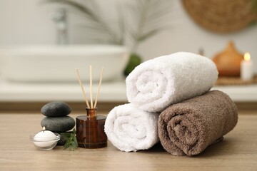 Spa composition. Rolled towels, aroma diffuser, massage stones and burning candle on wooden table indoors