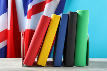 Learning foreign language. Different books on wooden table near flag of United Kingdom